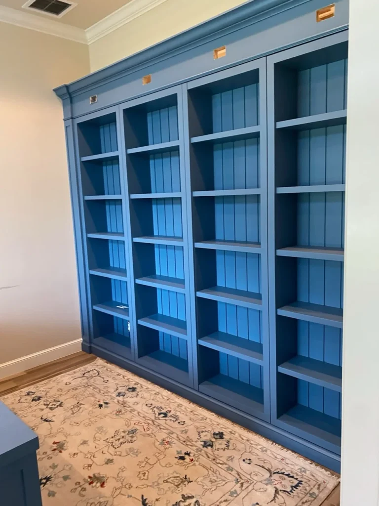 Floor-to-ceiling blue built-in library with beadboard backs and brass picture lights
