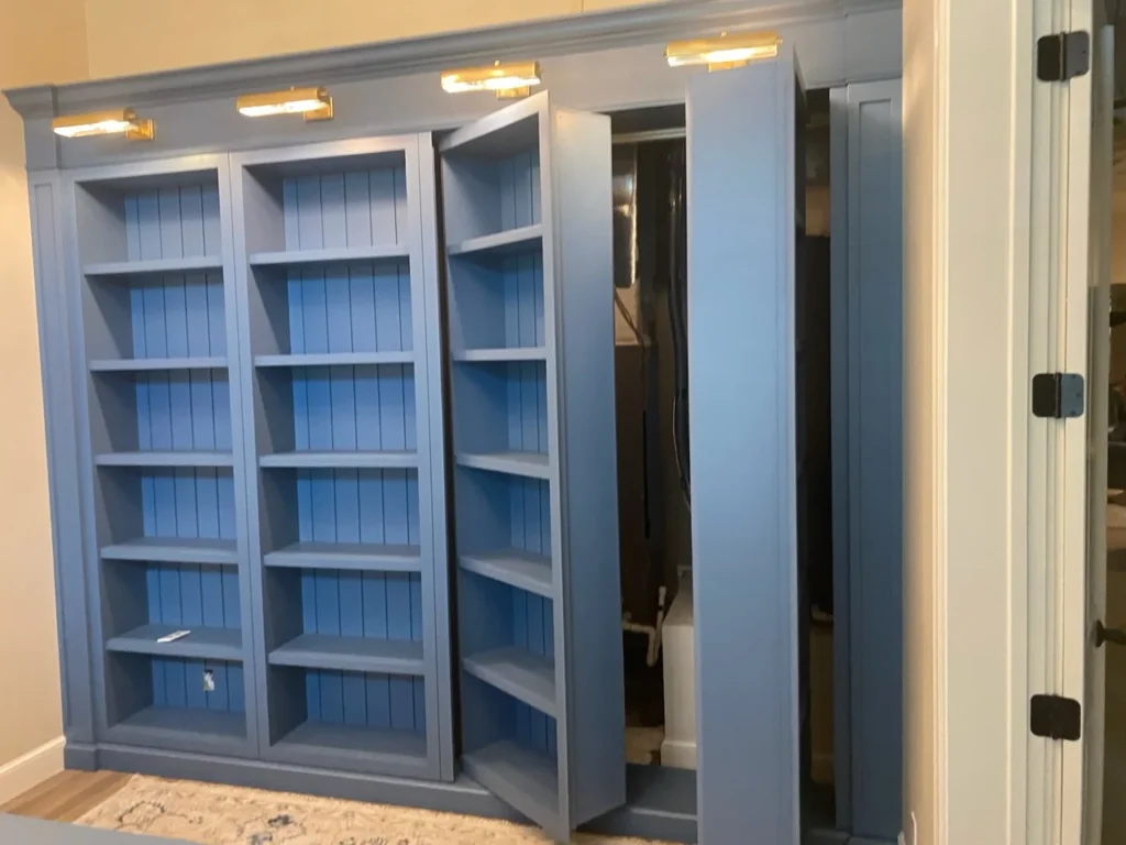 Blue built-in library with one shelving section opened as a concealed pivot door