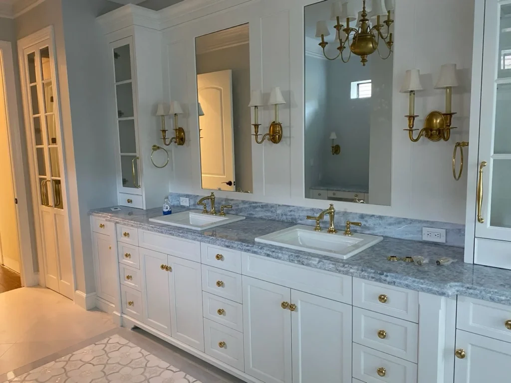 White double vanity with brass hardware, tall mirrored storage cabinets and stone counters