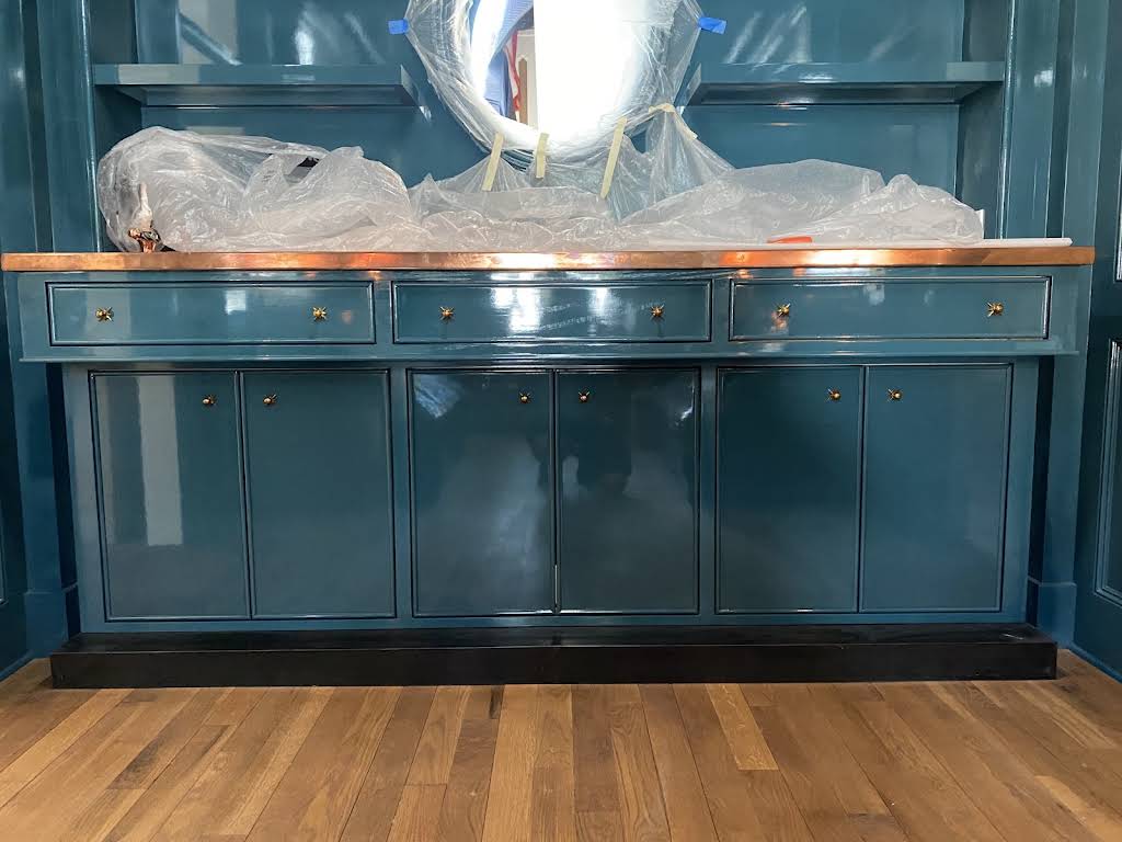 Deep teal built-in cabinetry with brass hardware and a warm wood counter