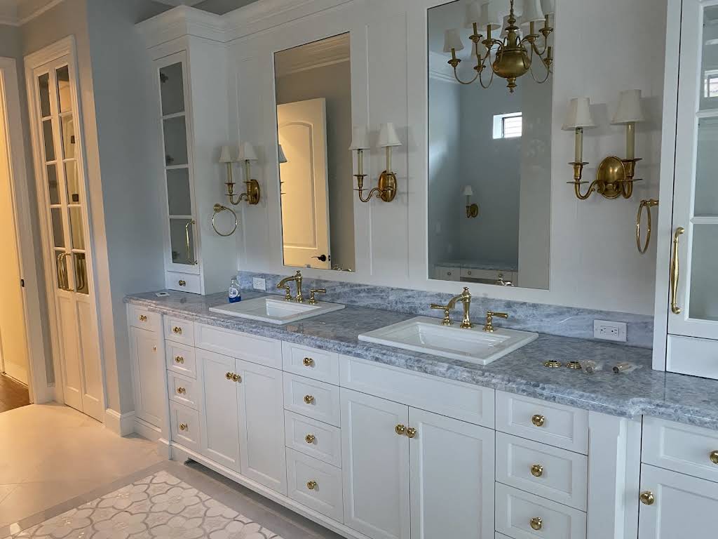 White custom double vanity with brass hardware, mirrored wall panels and stone counters