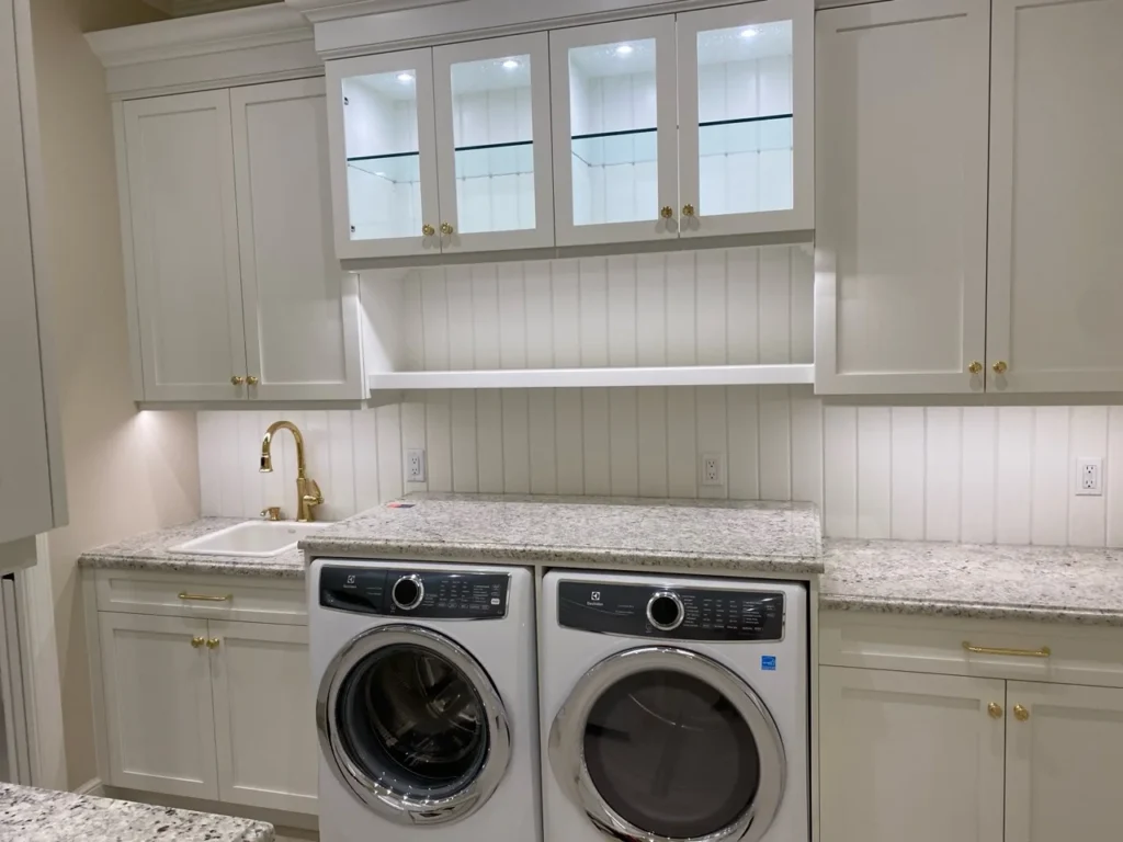 White laundry cabinetry with brass hardware, glass display doors and stone counters