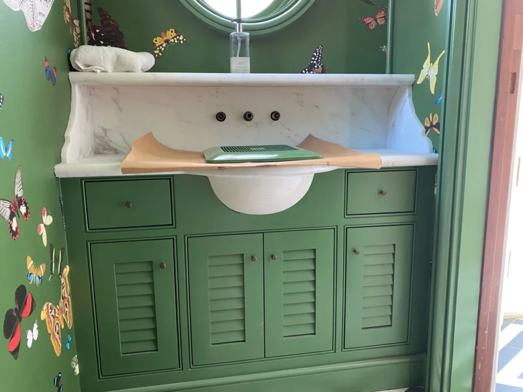 Green bathroom vanity with louvered doors and a marble sink surround