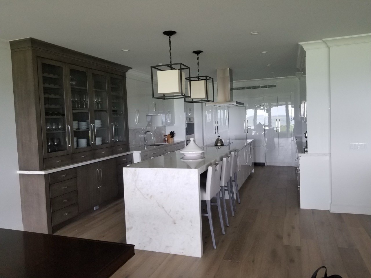 Modern white kitchen with a long waterfall island and contrasting dark display cabinetry