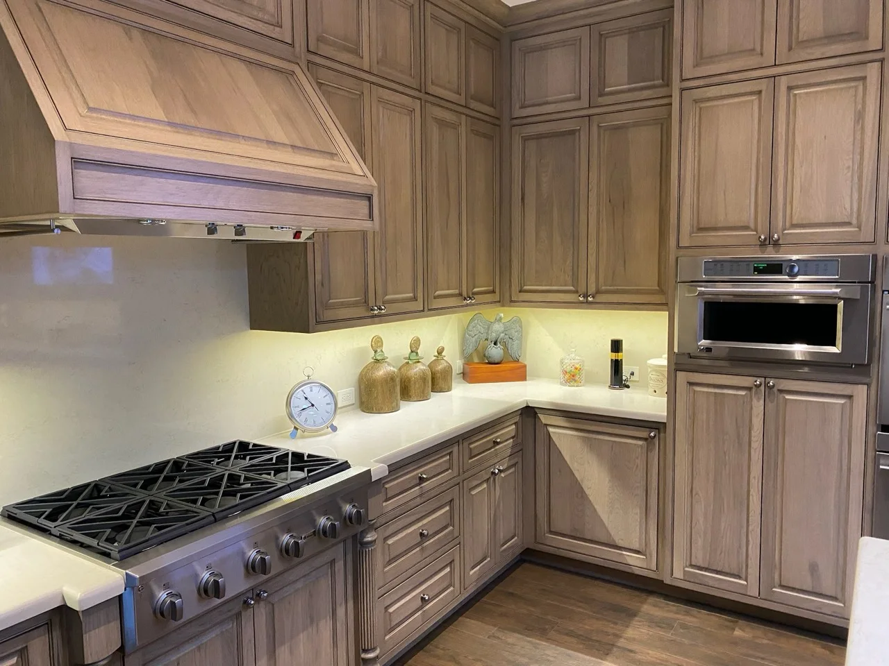 Stained manufactured kitchen cabinetry with paneled range hood and integrated storage