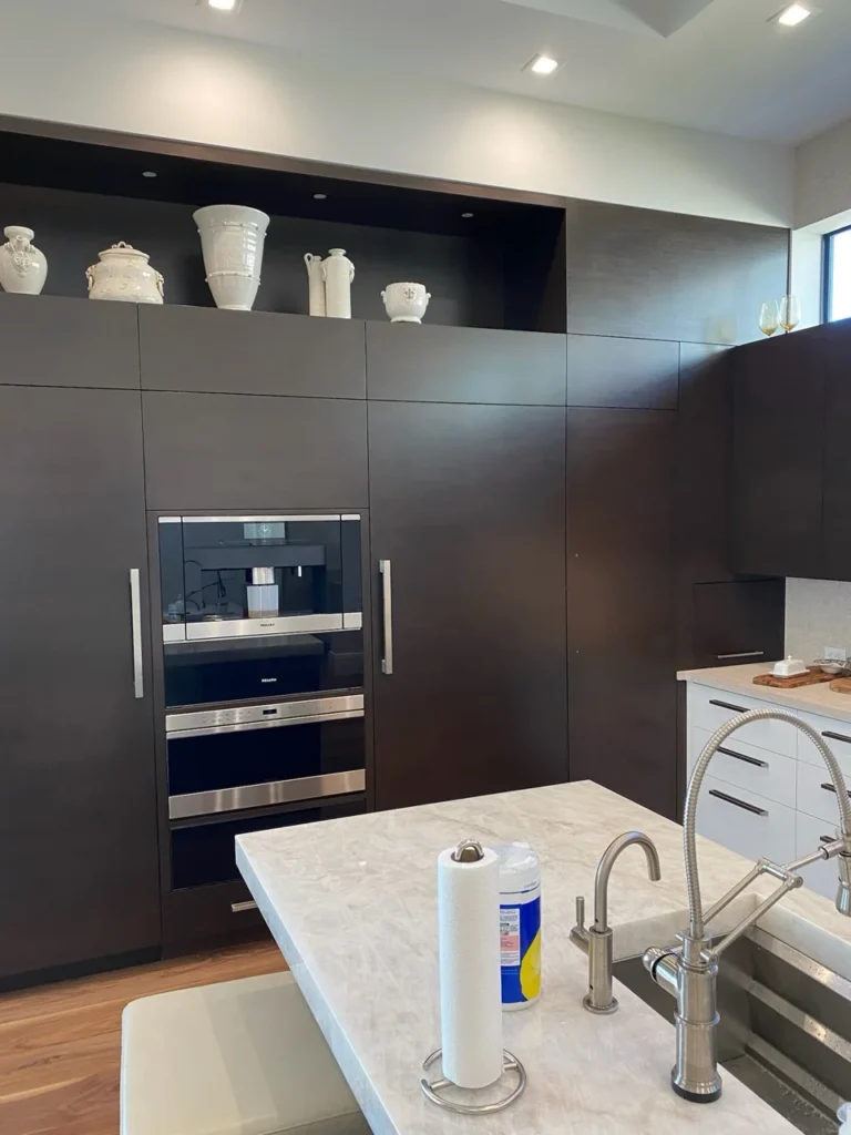 Modern kitchen with dark full-height cabinetry, integrated appliances and white stone island